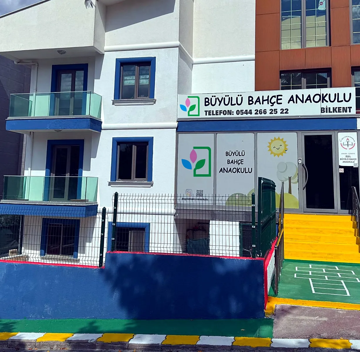 Büyülü Bahçe Anaokulu binası: tabela, logolu cam giydirme, sarı merdiven ve seksek